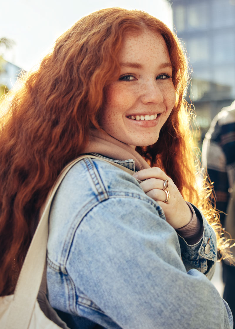 Person with long red hair, a jean jacket and bag over the shoulder