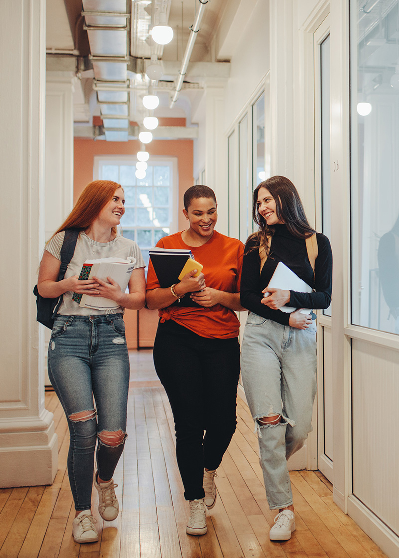Three students waling down a hallway carrying books and smiling